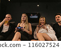 Female players battle on-screen while men watch in game room 116027524