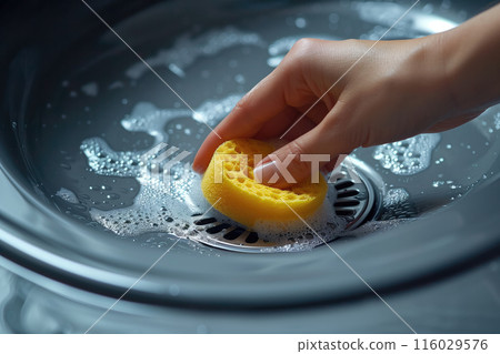 Hand holding a yellow sponge, scrubbing a sink with soapy water. Useful for promoting cleaning supplies and illustrating home cleaning techniques. 116029576