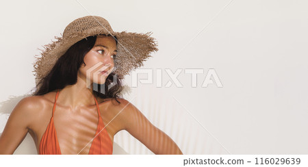 Woman in Red Bikini and Straw Hat Posing Against Sunlit Wall 116029639