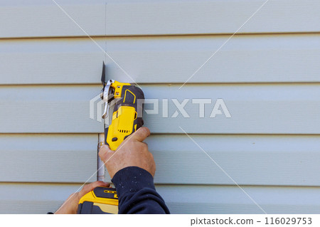 Reconstruction of house involves removal damaged vinyl siding with multi tool 116029753