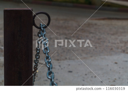 Fencing of a street parking lot with a shiny metal chain hanging on a welded ring to a concreted pole. The use of permanent types of joints in construction, welded seams. Fencing of a street parking lot with a shiny metal chain hanging on a welded ring to a concreted pole. The use of permanent types of joints in construction, welded seams. 116030319