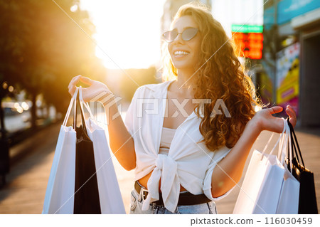 Stylish woman with shopping bags walks through city street. Consumerism, shopping, lifestyle concept 116030459