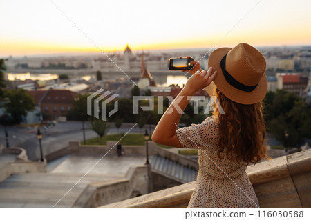 Young Woman on vacation using mobile phone to take photo of sunset of city. Rest, lifestyle concept. Young Woman on vacation using mobile phone to take photo of sunset of city. Rest, lifestyle concept. 116030588