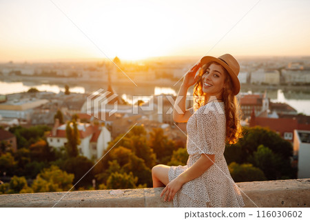Portrait of happy tourist in hat at dawn enjoys cityscape. Traveling in Europe. Concept tourism. 116030602