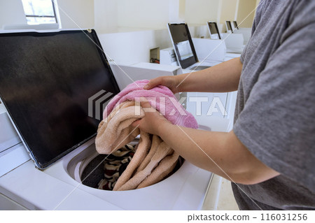 An attendant washes towels at laundromat with washing machine An attendant washes towels at laundromat with washing machine 116031256