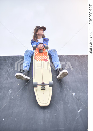 Girl having fun riding skateboards at skate park, Portrait of smiling young female skateboarder holding her skateboard. Recreational Activity Concept. 116031607