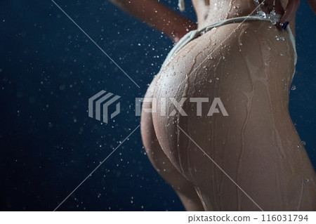 A woman's buttocks in close-up with water droplets on her body. Cropped image of a young woman on a dark blue background. With space to copy. High quality photo 116031794