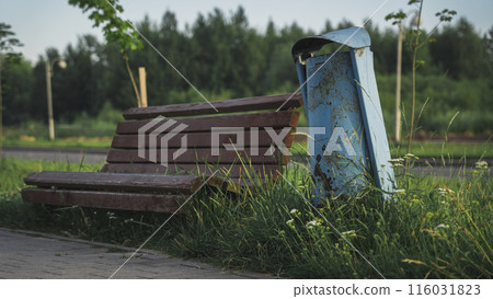 An old wooden bench next to a blue trash can 116031823