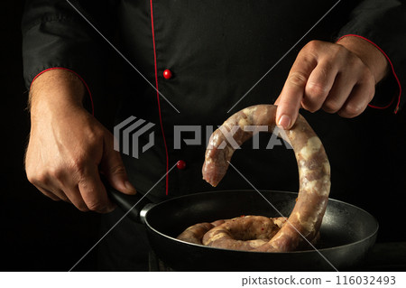 The cook puts the sausage in the frying pan with his hand. Cooking or frying sausage in the kitchen at home 116032493