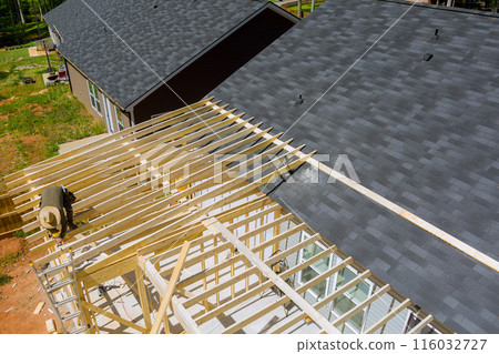 An unfinished residential home under construction is framed out with wooden beam supports An unfinished residential home under construction is framed out with wooden beam supports 116032727