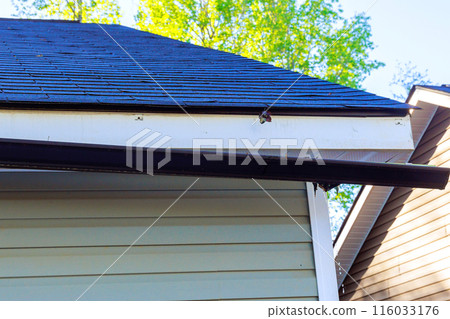 Broken rain gutter on roof of house after hurricane damages Broken rain gutter on roof of house after hurricane damages 116033176