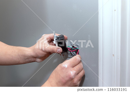 During renovations, professional electrician connects an electric socket in wall of home 116033191