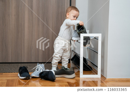 Little child playing with adult footwear in hallway. Concept of toddlers joyful exploration and mischief Little child playing with adult footwear in hallway. Concept of toddlers joyful exploration and mischief 116033365