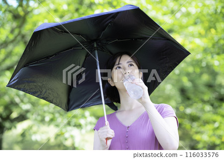 A woman with a parasol hydrates herself among the fresh greenery A woman with a parasol hydrates herself among the fresh greenery 116033576