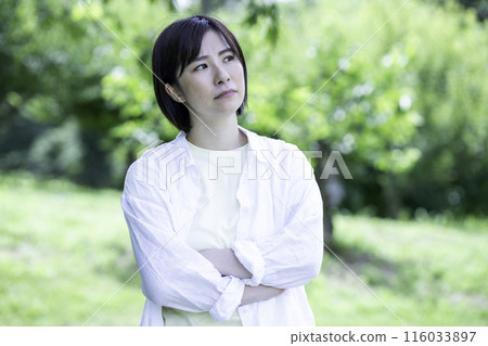Dissatisfied woman in a park with fresh green leaves Dissatisfied woman in a park with fresh green leaves 116033897