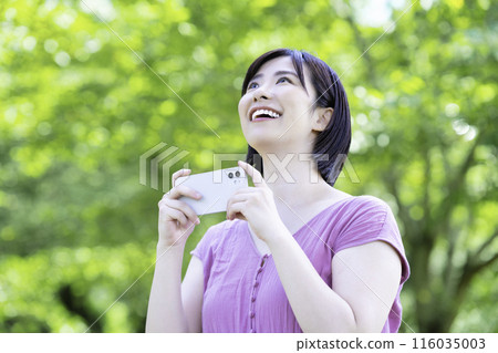 A woman taking a smartphone photo in the fresh greenery 116035003