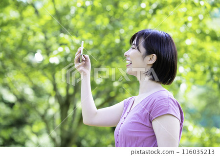 A woman taking a smartphone photo in the fresh greenery A woman taking a smartphone photo in the fresh greenery 116035213