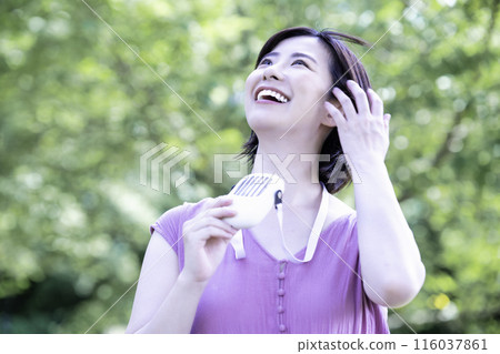 一位年輕女子在新鮮的綠色公園裡用便攜式風扇降溫 116037861