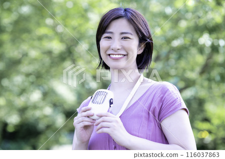 一位年輕女子在新鮮的綠色公園裡用便攜式風扇降溫 116037863