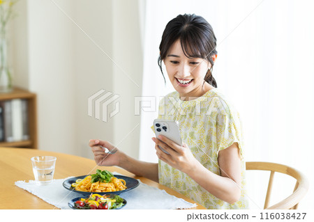 年輕女子在家吃義大利麵時看著智慧型手機 年輕女子在家吃義大利麵時看著智慧型手機 116038427