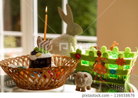 Easter cake with a lit candle. Easter colorful eggs in a basket on the table 116038676