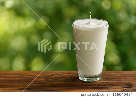 glass of milk with splash and drop on table with green garden on the background glass of milk with splash and drop on table with green garden on the background 116040484