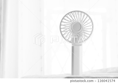 A monochrome handheld fan by the window 116041574