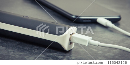 Black smartphone with connected plug of external powerbank. Mobile phone charging 116042126
