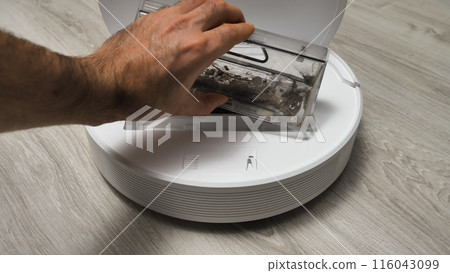 A hand empties a robot vacuum's dust collector into a trash can. 116043099