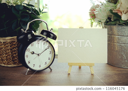 Empty card space for text message with wooden easel and alarm clcok on wooden background Empty card space for text message with wooden easel and alarm clcok on wooden background 116045176