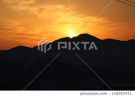 Morning landscape with orange clouds in the blue sky and the sun rising over the black silhouetted mountain range Morning landscape with orange clouds in the blue sky and the sun rising over the black silhouetted mountain range 116047431