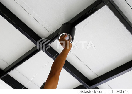 Hand of an electrician installing a light on the ceiling. 116048544