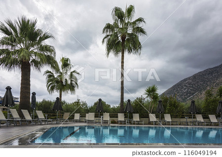 Outdoor swimming pool with sunbeds and umbrellas in cloudy weather Outdoor swimming pool with sunbeds and umbrellas in cloudy weather 116049194