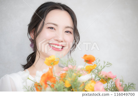 Cosmetic and beauty portrait of a young woman holding a bouquet of flowers, orange and pink image, looking at camera 116049700