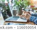 A person using a smartphone while working on a laptop at a cozy cafe. by Generative AI 116050054