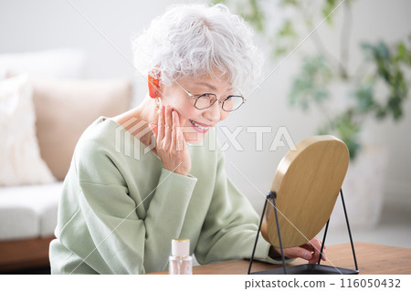 Senior woman looking at the mirror and taking care of her skin (skin care) 116050432