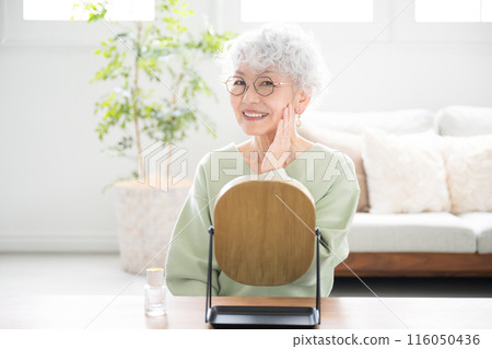 Front view of senior woman looking at mirror, touching cheek, taking care of skin (skin care), looking at camera 116050436
