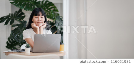 Young woman working on a laptop at home office with green plants in the background, showcasing a casual and relaxed atmosphere, ideal for remote work and freelancing concepts. Young woman working on a laptop at home office with green plants in the background, showcasing a casual and relaxed atmosphere, ideal for remote work and freelancing concepts. 116051981