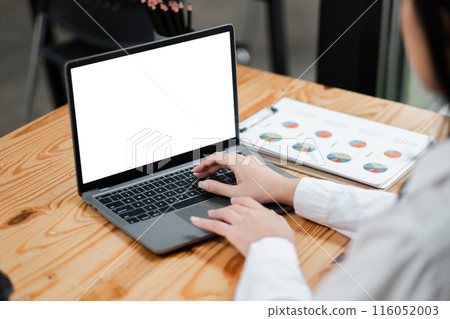 Close-up of hands typing on a laptop with a blank screen, business charts on paper, modern office setting, productivity and technology. Close-up of hands typing on a laptop with a blank screen, business charts on paper, modern office setting, productivity and technology. 116052003