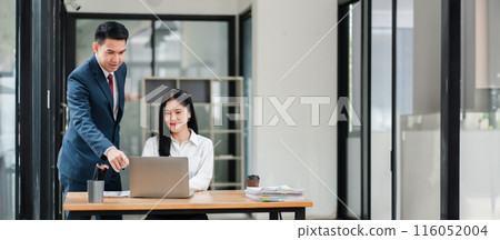Two business professionals in a modern office, collaborating on a project. Man in suit and woman in white shirt working together at a desk with a laptop. Two business professionals in a modern office, collaborating on a project. Man in suit and woman in white shirt working together at a desk with a laptop. 116052004