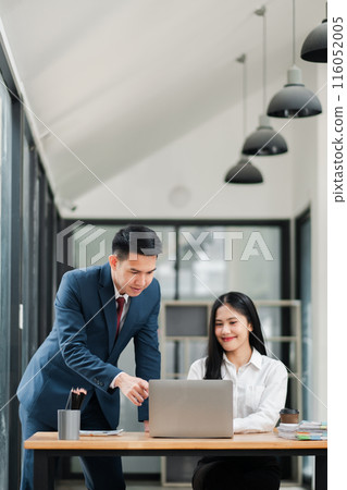 Businessman and businesswoman collaborating on a project in a modern office, using a laptop and discussing ideas. Businessman and businesswoman collaborating on a project in a modern office, using a laptop and discussing ideas. 116052005