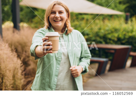 Coffee to go at autumn park. Food, rest, Take away concept. Place logo on mug, mockup. Woman hand holding brown paper cup on park background 116052569