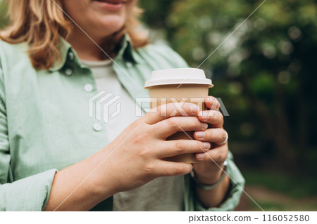 Coffee to go at autumn park. Food, rest, Take away concept. Place logo on mug, mockup. Woman hand holding brown paper cup on park background 116052580
