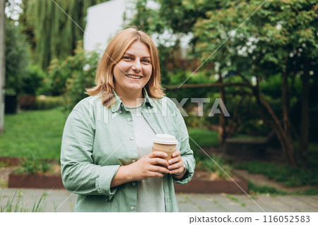 Happy redhead 30s Woman holding brown paper cup of coffee on public park background, Coffee to go on the city street. Food, rest, Take away concept. 116052583