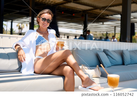 young girl in summer dress and swimwear resting at the sunny beach, sitting at a cafe with a young girl in summer dress and swimwear resting at the sunny beach, sitting at a cafe with a 116052742