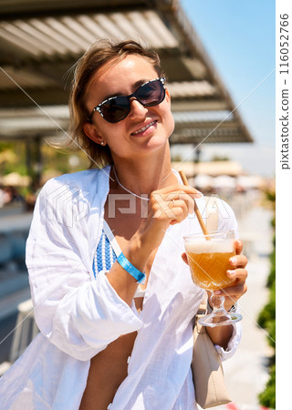 young girl in summer dress and swimwear resting at the sunny beach, sitting at a cafe with a young girl in summer dress and swimwear resting at the sunny beach, sitting at a cafe with a 116052766