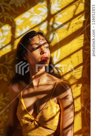 A woman in a yellow dress is standing in front of a yellow wall 116052855