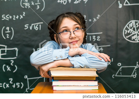 A schoolgirl girl put her hands and head on a stack of books in a school class 116053413