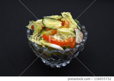Vegetable salad in a glass salad bowl on a black background. A portion of vegetable salad. 116055732