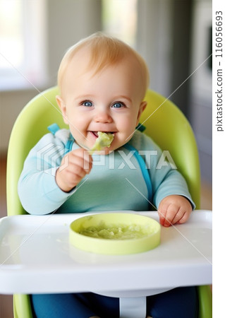 A baby smiling at the table, grabbing food with a spoon from a bowl 116056693